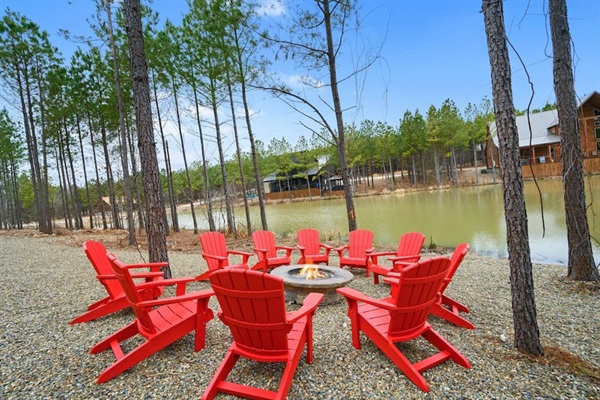A cozy fire pit area with red Adirondack chairs overlooks a lakefront retreat, perfect for outdoor seating and evening gatherings. Enjoy storytelling and marshmallow roasting in this cabin rental, designed for family-friendly vacations and relaxation.