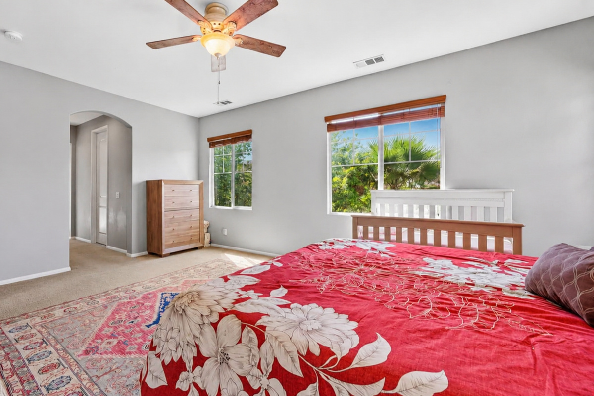 Primary bedroom with soft bedding, ceiling fan, dresser storage, and peaceful window views.