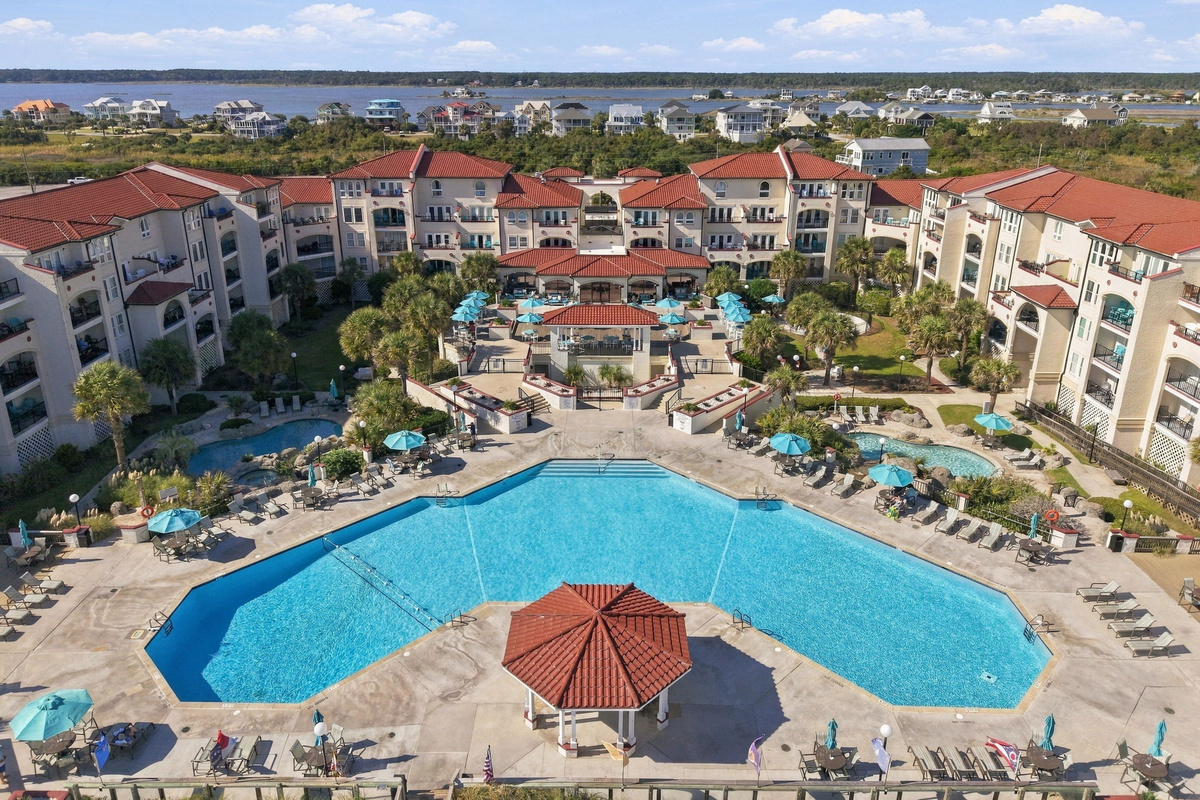 Resort-style pool complex with a central swimming pool, gazebo, sun loungers, and surrounding terracotta-roofed residences.