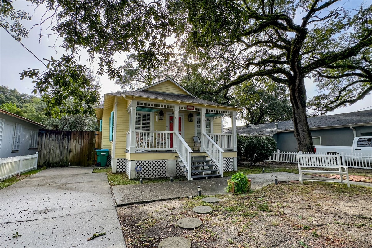 Quaint beach cottage nestled under mature trees, featuring a cozy porch and a quiet, relaxed setting.