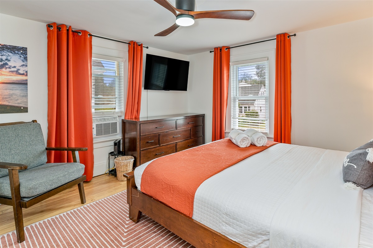 Spacious king bedroom with vibrant orange accents, smart TV, and lots of natural light for a cozy, modern retreat. Bedroom #1 upstairs 