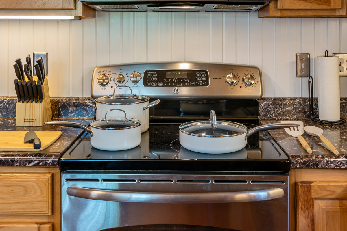 Meal preparation is a breeze with this premium ceramic nonstick pots and pans set complete with glass lids. The kitchen comes fully stocked with essential cooking utensils, a chef's knife, a wooden cutting board, and a glass-top electric stove.