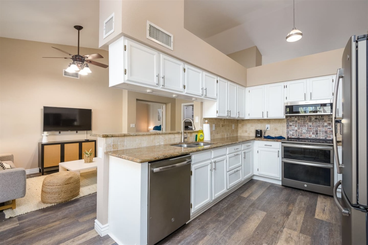 Full kitchen with stainless steel appliances, dishwasher, granite counters, and open access to the living room.