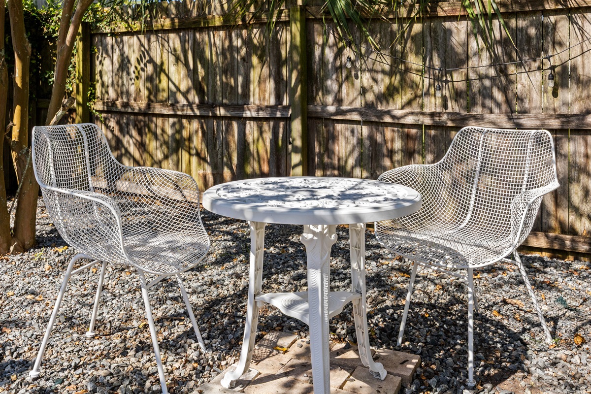Cozy Bistro Seating
A quaint outdoor seating nook with white metal chairs and a matching table, set against a wooden fence with string lights. A peaceful spot for morning coffee or evening conversation.