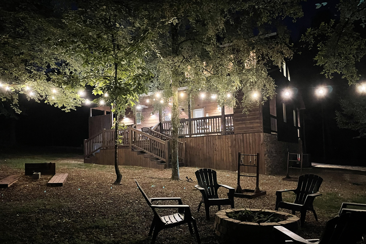Beautiful back yard illuminated with overhead party lights to enjoy outdoor games and the fire pit.