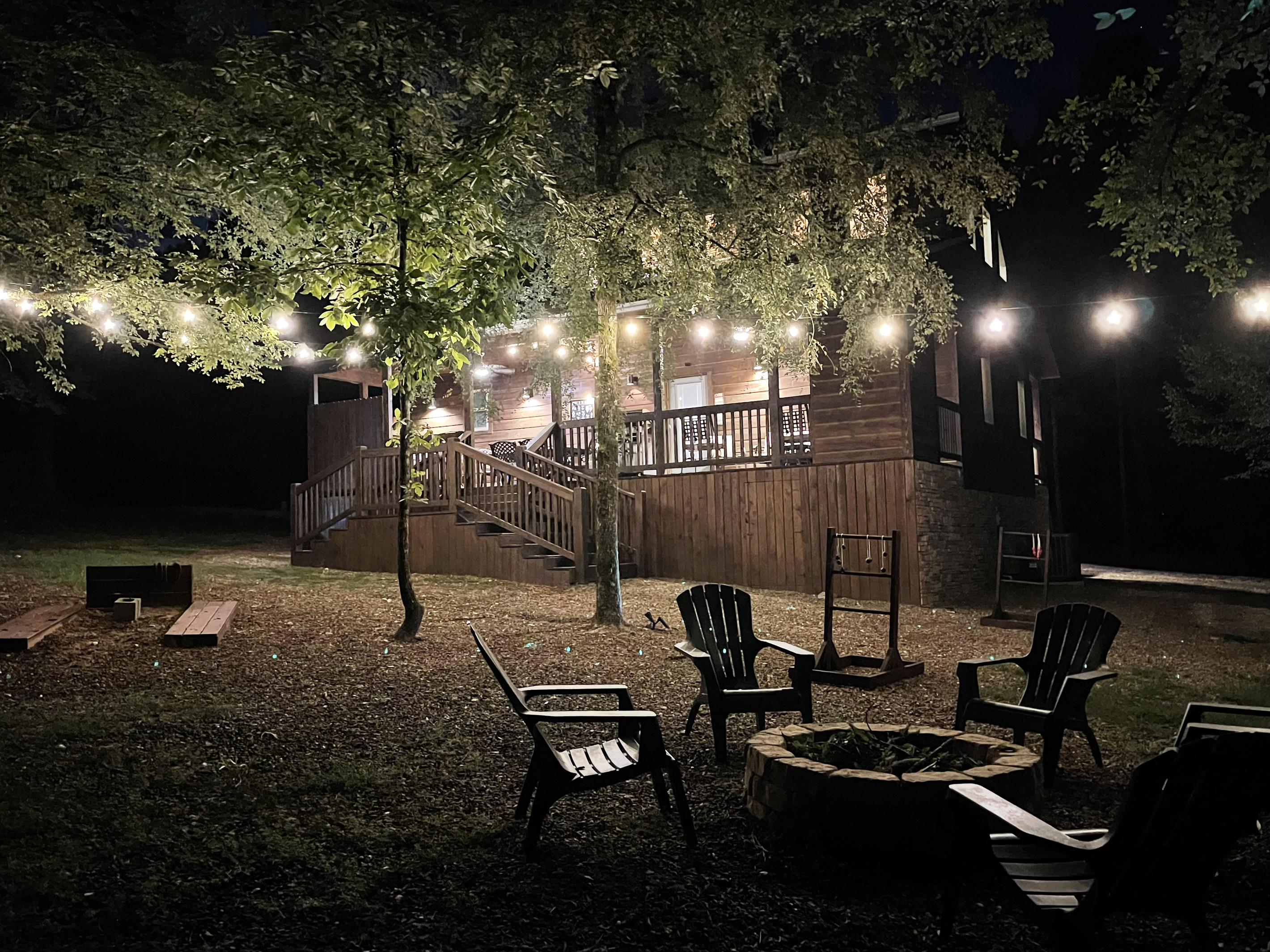 Beautiful back yard illuminated with overhead party lights to enjoy outdoor games and the fire pit.