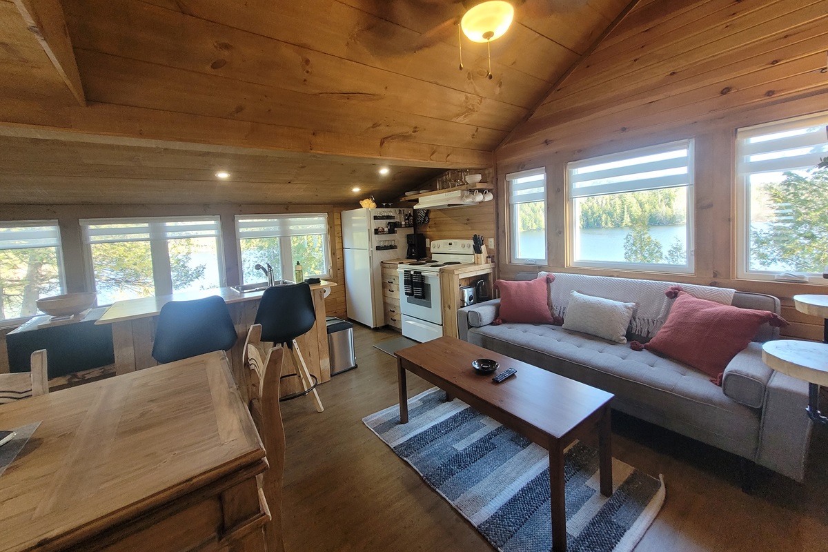 Living room couch and kitchen area show views of lake through the many windows