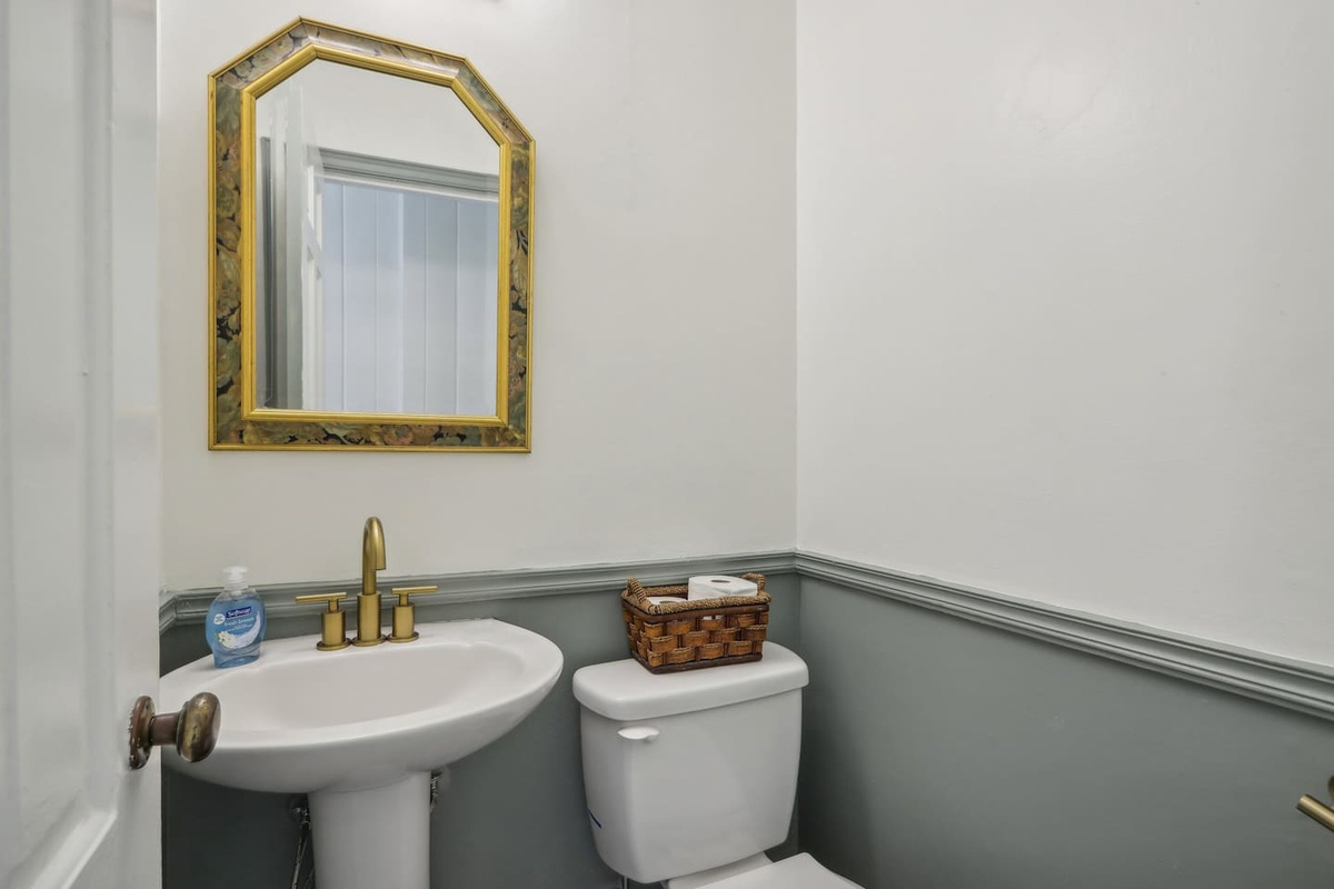 A convenient half bathroom with a pedestal sink, toilet, and elegant gold accents.