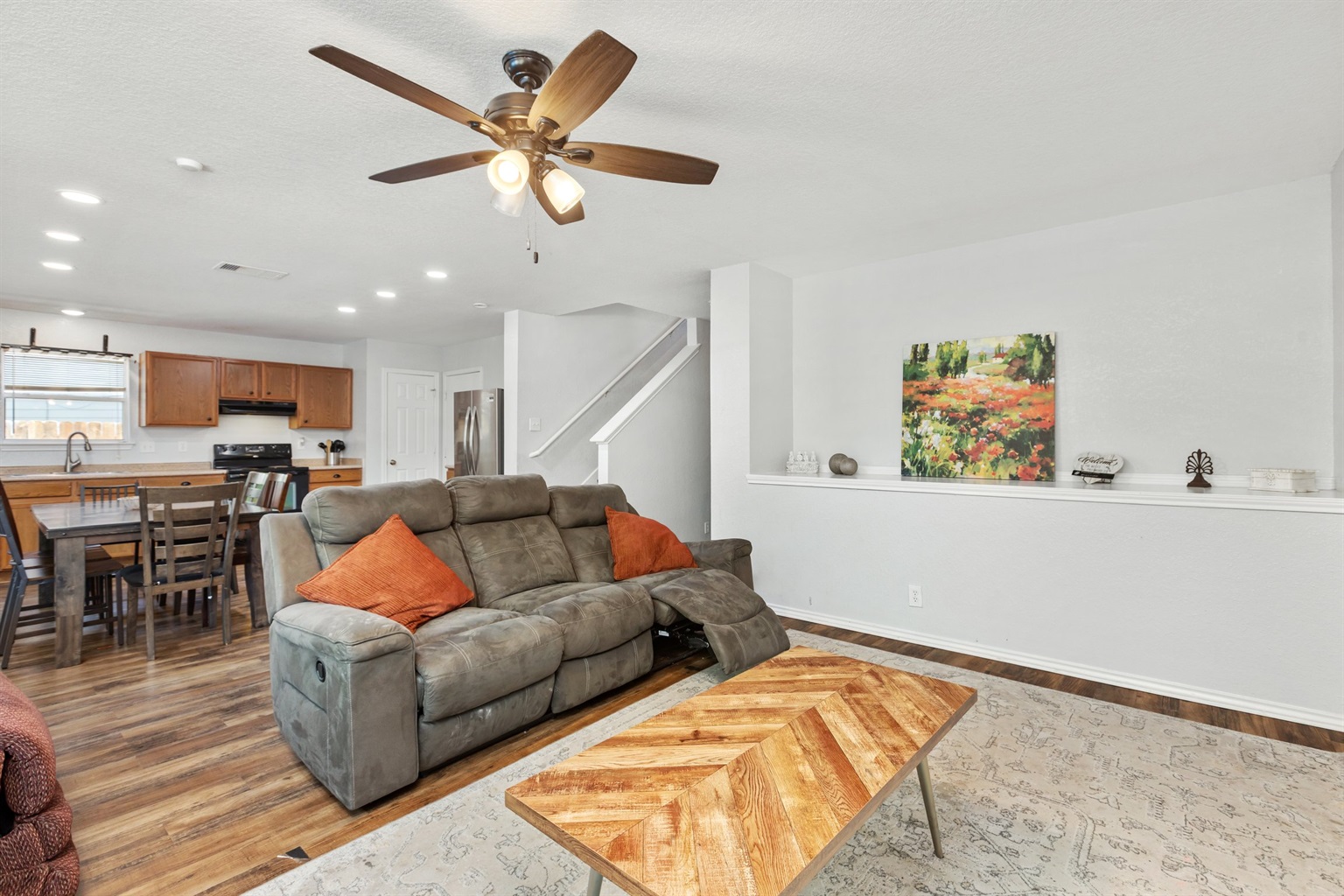 Main floor open-concept layout connecting living room, dining, and kitchen. Hardwood floors, ceiling fan, and reclining sectional seating throughout. Built for families and groups in Northeast San Antonio.