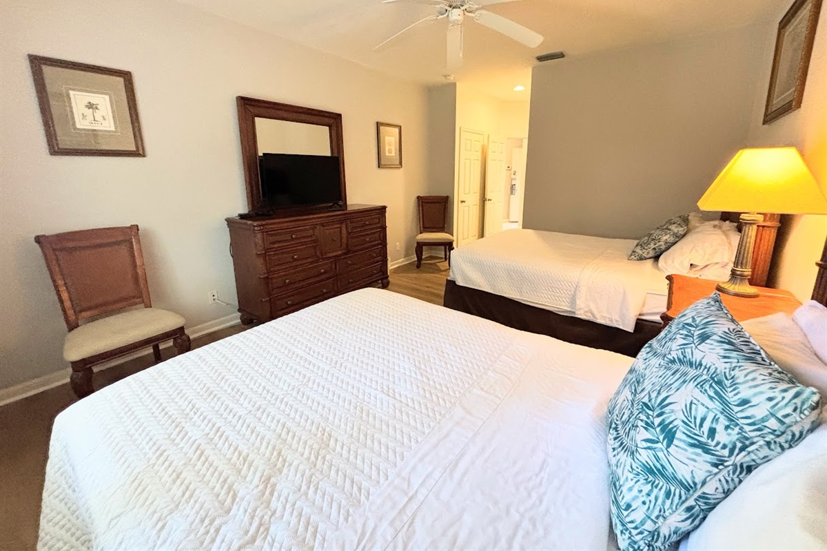 Spacious bedroom with two beds, dresser storage, ceiling fan, and a clean, relaxing layout.