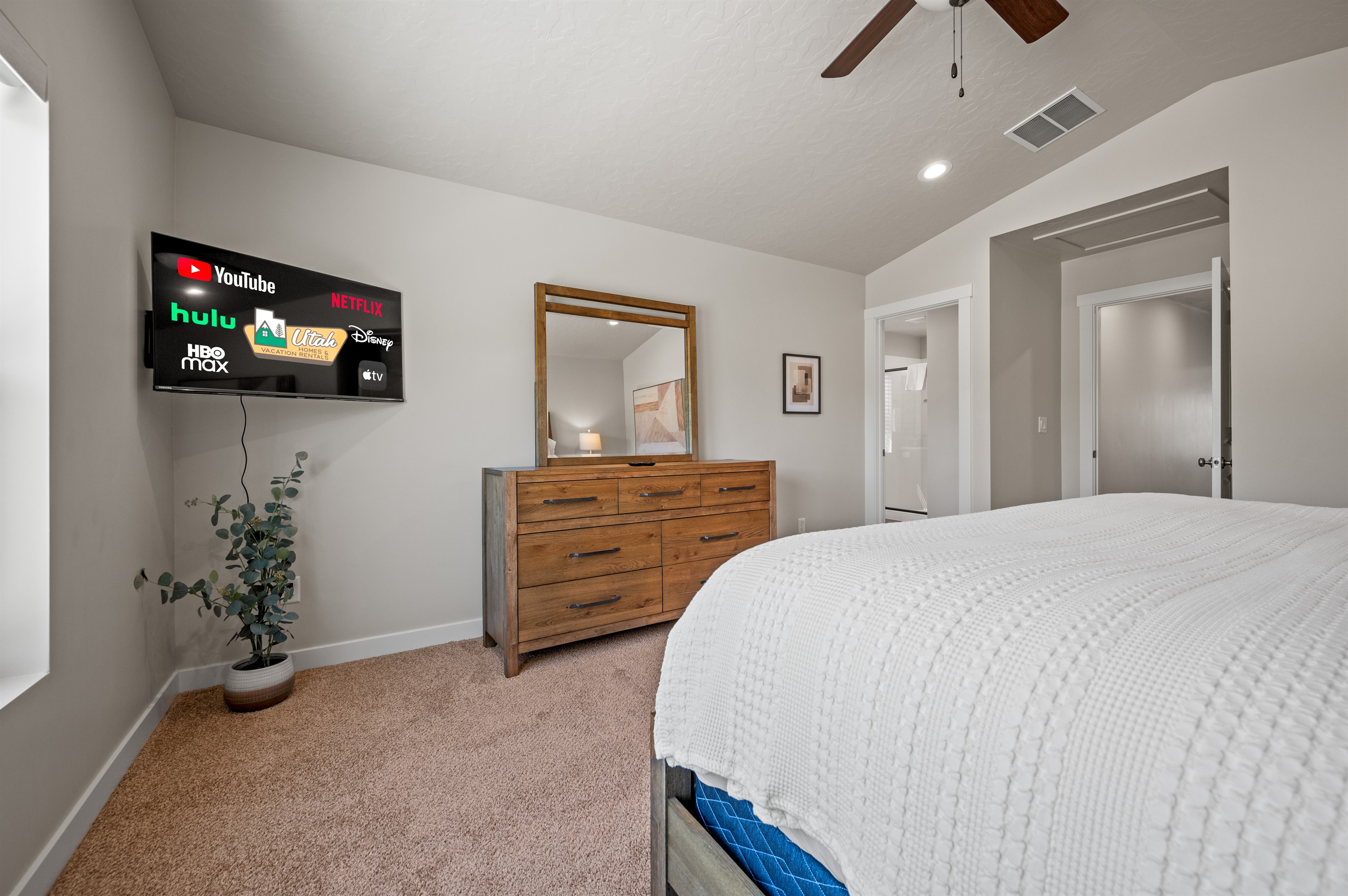 The primary bedroom offers comfort and style with a large TV, ceiling fan, elegant dresser, and luxurious bedding—your private retreat after a day of adventure.