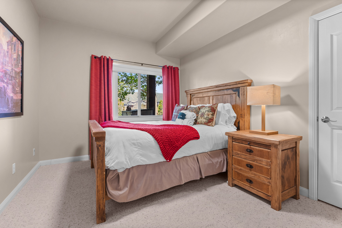 Comfortable downstairs queen bedroom with warm wood furnishings, soft bedding, and a peaceful space to relax after a day exploring Pineview Reservoir and the mountains.