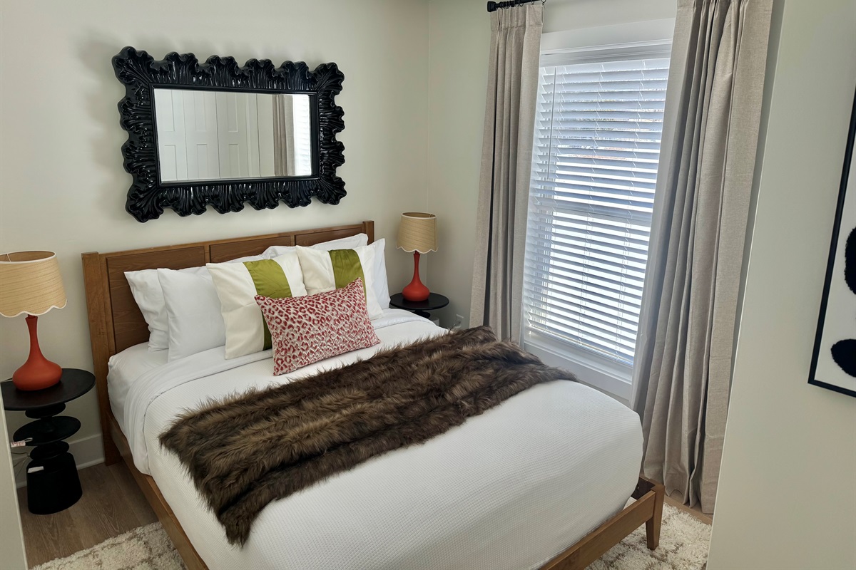 Cozy bedroom featuring a plush queen bed with professionally laundered linens, blackout curtains, and a noise machine for a restful night’s sleep. Thoughtfully styled with warm touches and natural light to help you relax and unwind.