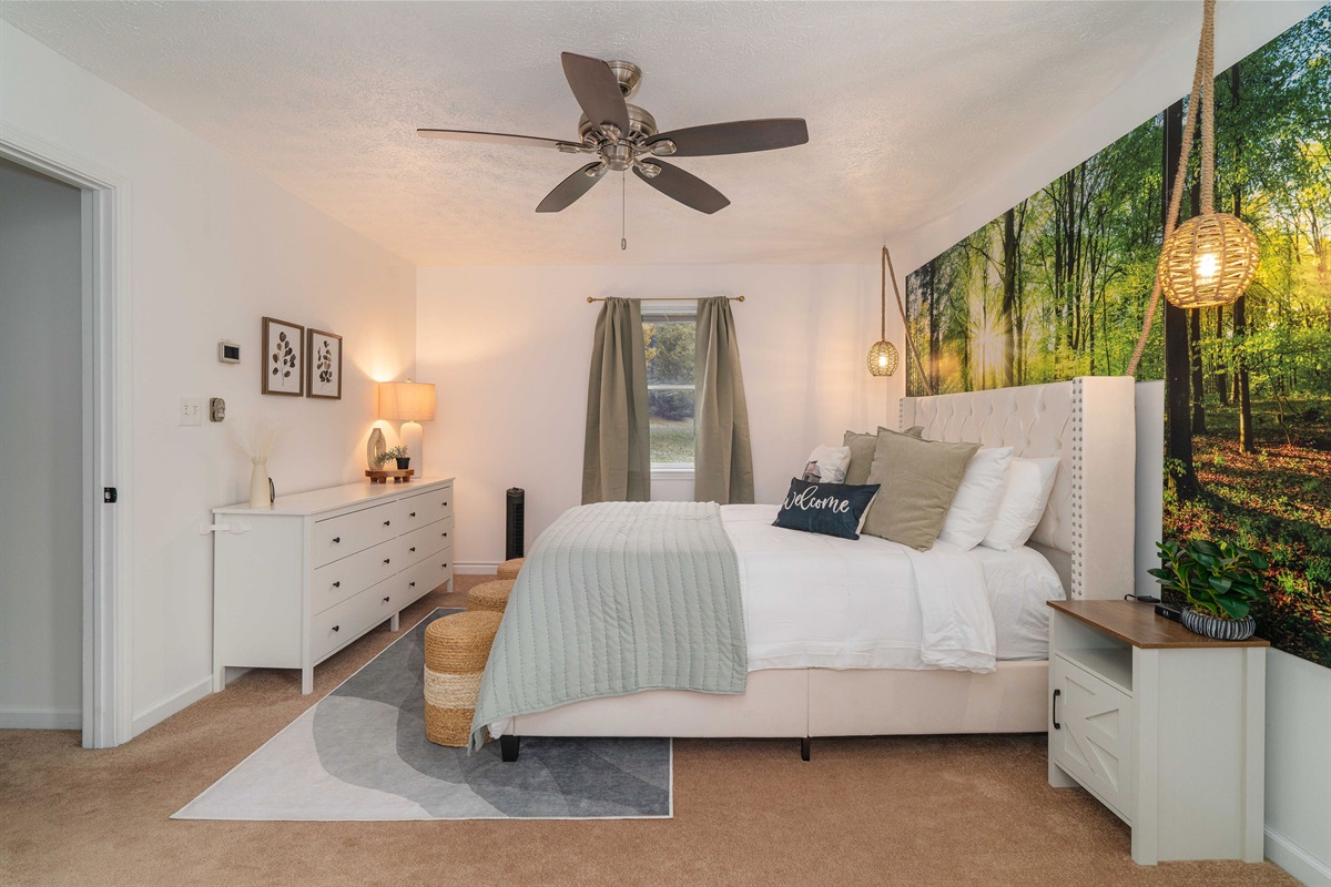 Spacious primary bedroom with Woodland Sunrise feature wall, queen bed, plush linens, and peaceful forest views.
