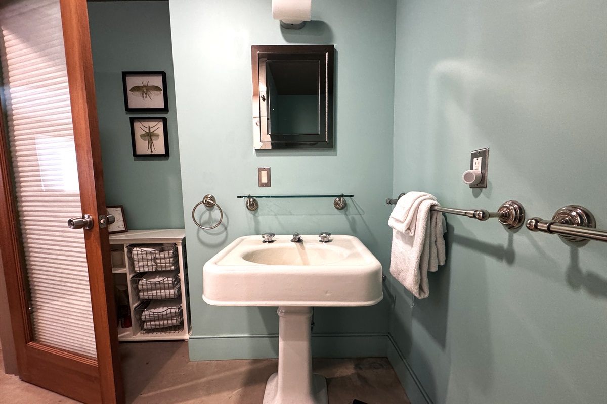 Lower-level bathroom featuring a classic pedestal sink and ample storage for fresh linens. The modern door with integrated built-in blinds ensures total privacy while maintaining the home’s clean, functional aesthetic.
