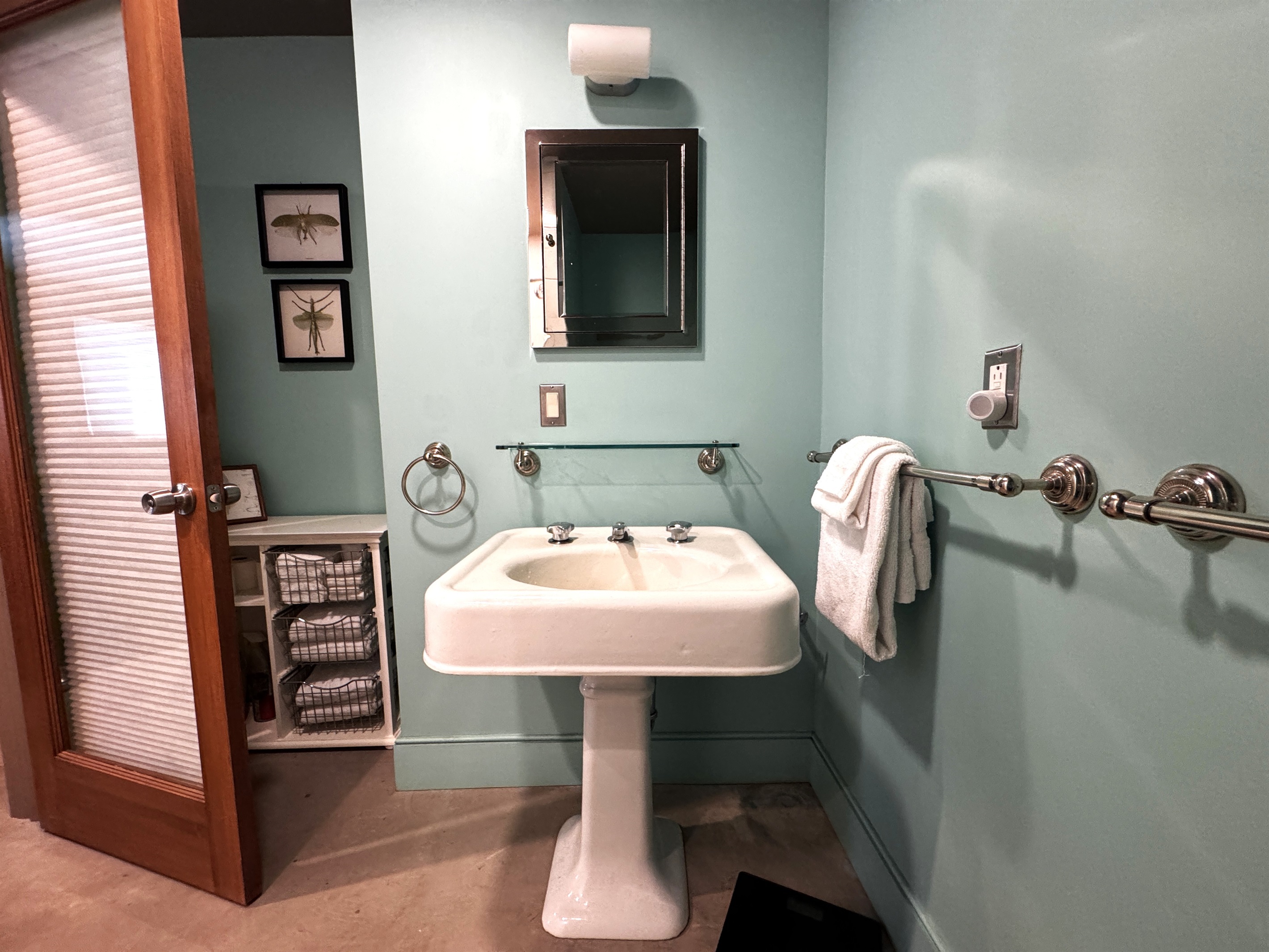 Lower-level bathroom featuring a classic pedestal sink and ample storage for fresh linens. The modern door with integrated built-in blinds ensures total privacy while maintaining the home’s clean, functional aesthetic.