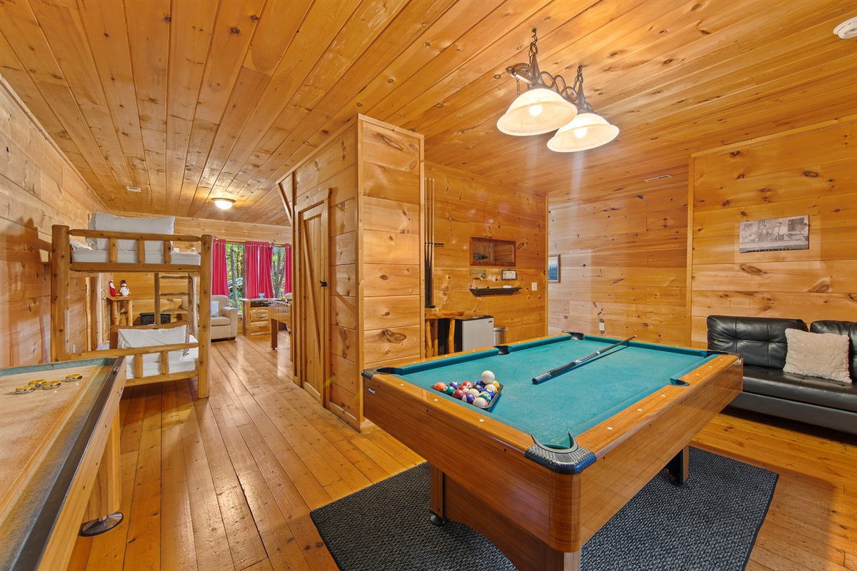 The game room also offers a pool table with vibrant green felt and a shuffleboard table. Large windows bring in natural light and connect the space to the outdoors.