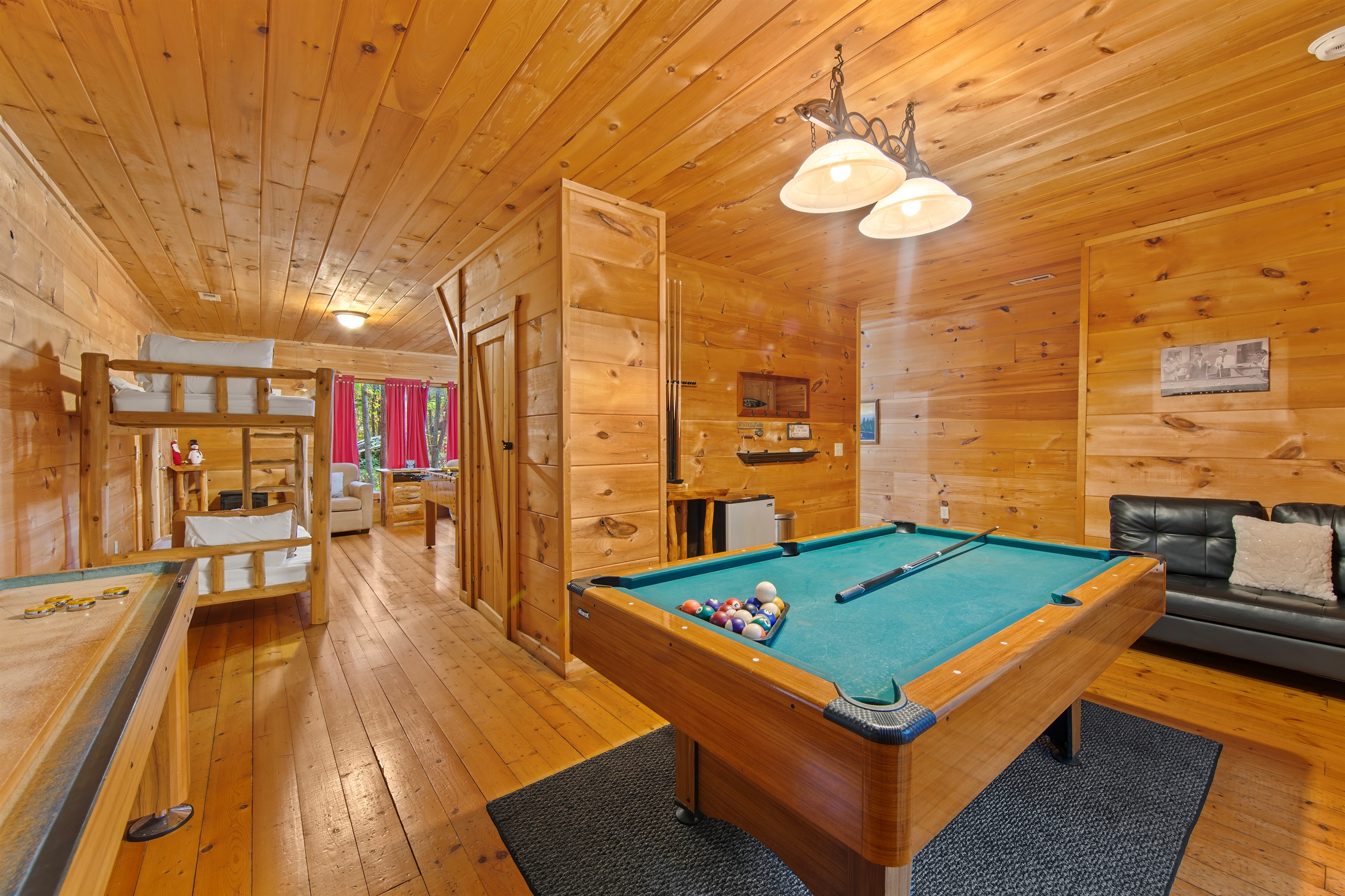 The game room also offers a pool table with vibrant green felt and a shuffleboard table. Large windows bring in natural light and connect the space to the outdoors.