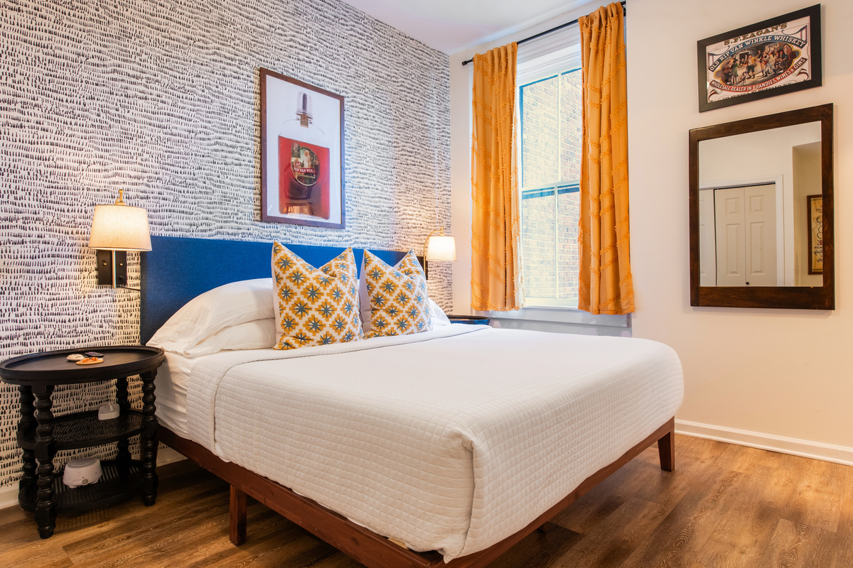 The bedroom, with a blue upholstered headboard and yellow curtains.