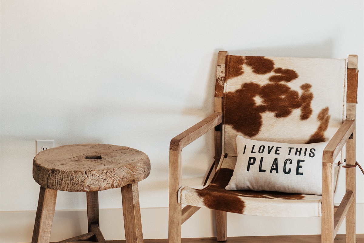 A welcome corner inside the Lazy Spur Suite — a leather chair, a wooden stool, and a handcrafted welcome pillow at Gaines Ranch on the Square.