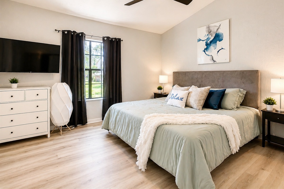 Comfortable bedroom featuring queen bed, large window with natural light, and ceiling fan for guest comfort.