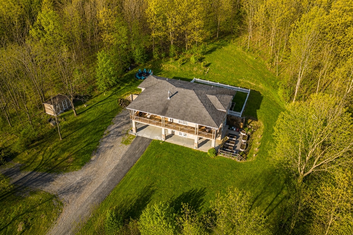This aerial view showcases a stunning, modern home surrounded by lush greenery, featuring expansive outdoor living spaces and a serene setting, perfect for a luxurious retreat. 