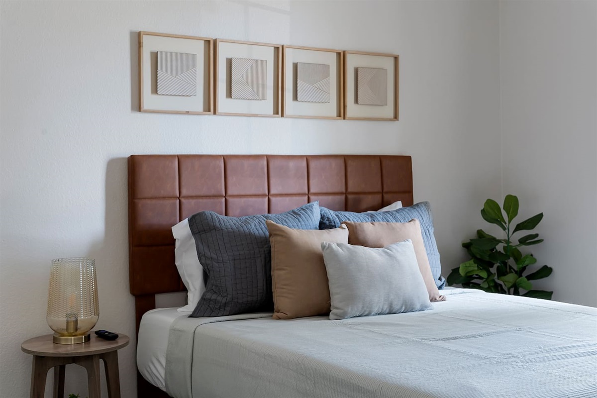 Welcome to our tranquil bedroom featuring a queen bed, softly illuminated by a side table lamp, with sunlight streaming through the window.