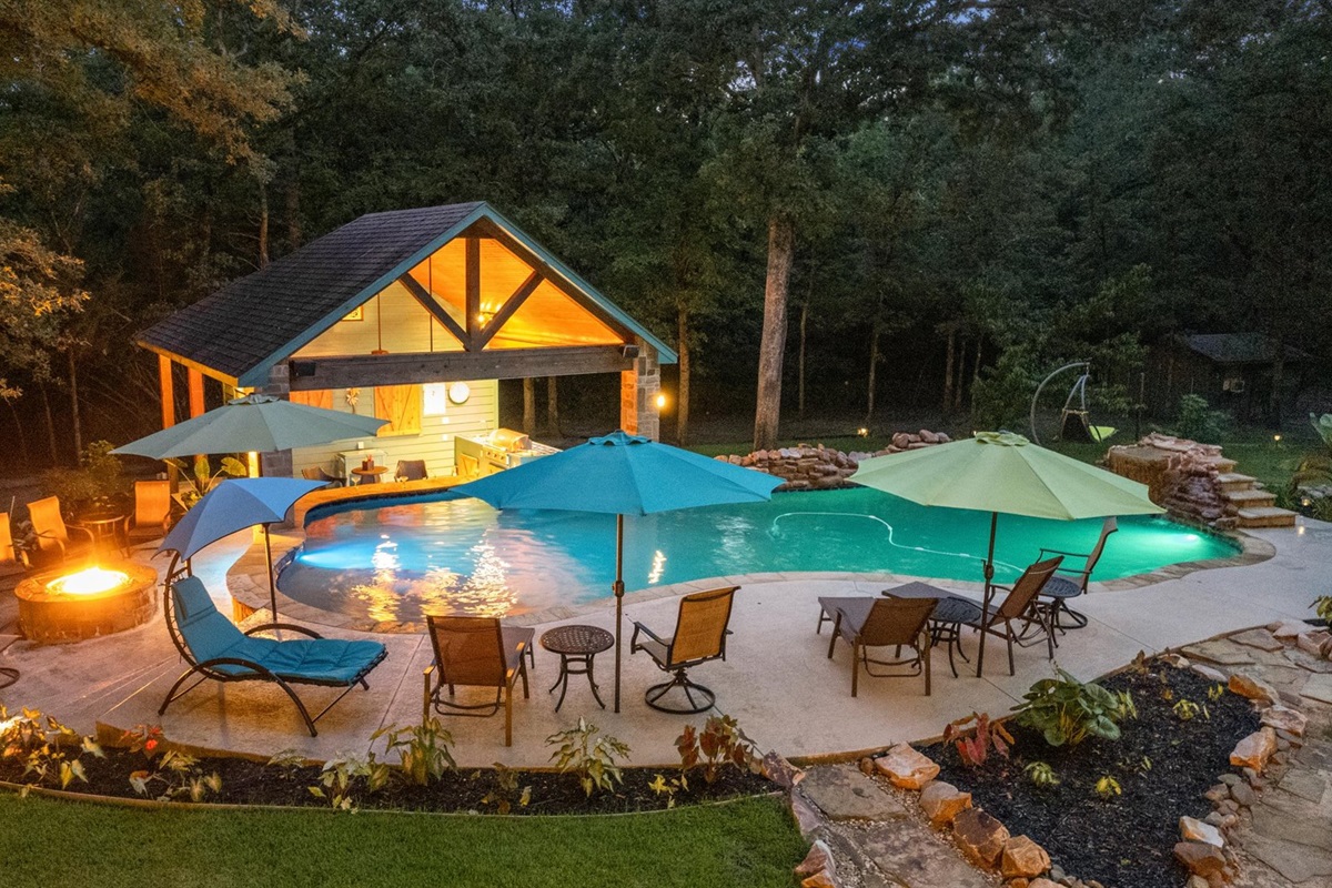 A stunning backyard oasis at night! Relax by the glowing fire pit, lounge by the pool, or enjoy the cozy ambiance of the illuminated outdoor kitchen and swim-up bar—perfect for unwinding under the stars