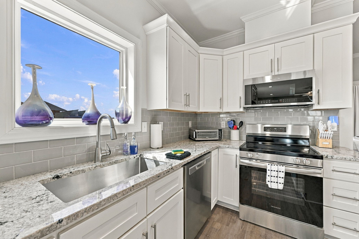 Detailed view of the gourmet kitchen space highlighting the undermount stainless steel sink with a goose-neck faucet, grey subway tile backsplash, polished granite counter space, and stainless steel range oven setup.