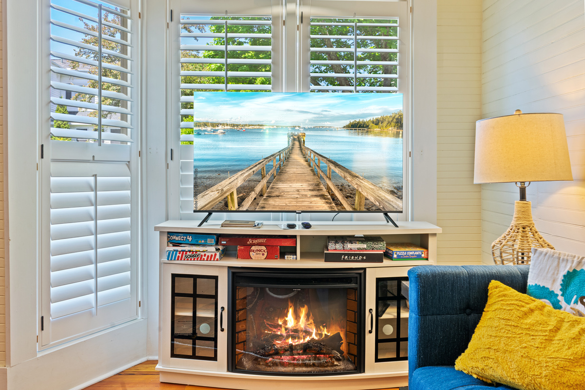 The heart of the upper-level "Quarterdeck" entertainment center. An electric fireplace glows beneath the new 50-inch Roku Smart TV, while the shelves stand fully stocked with classic board games for family tournament nights at the end of the day.