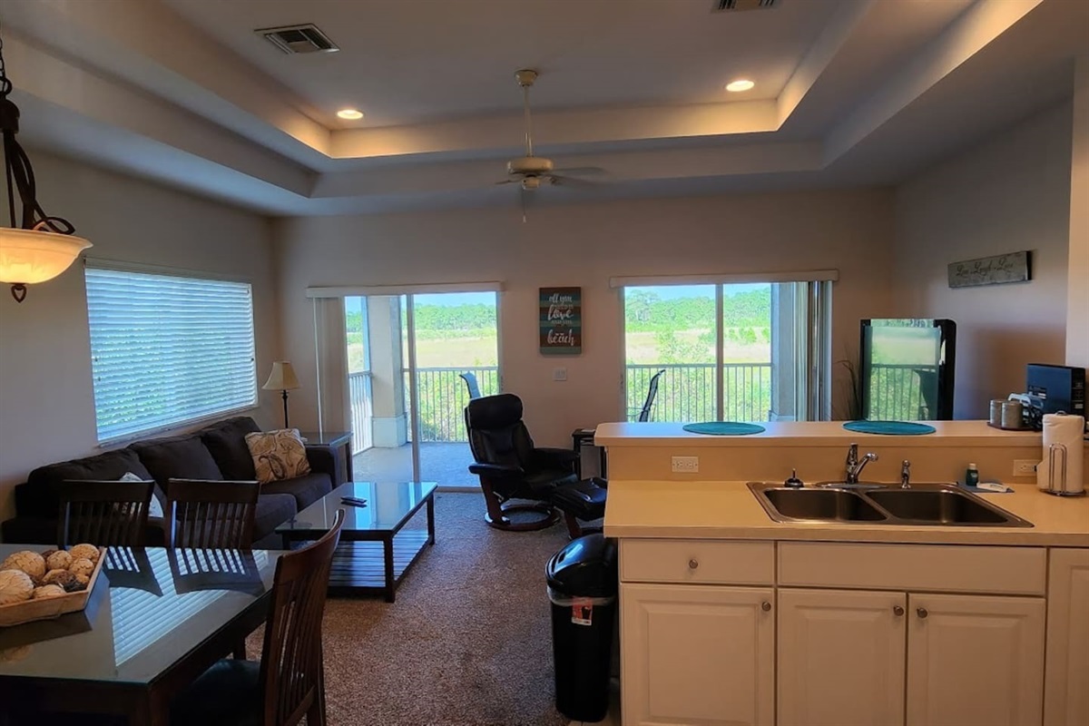 Open living area featuring high ceilings, comfortable seating, and natural light from large windows and balcony doors.