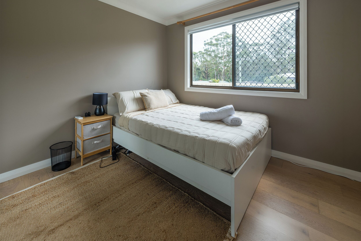 This bedroom at Luna’s Sanctuary features a comfortable bed, ceiling fan, bedside storage and a wide window with leafy outlooks.