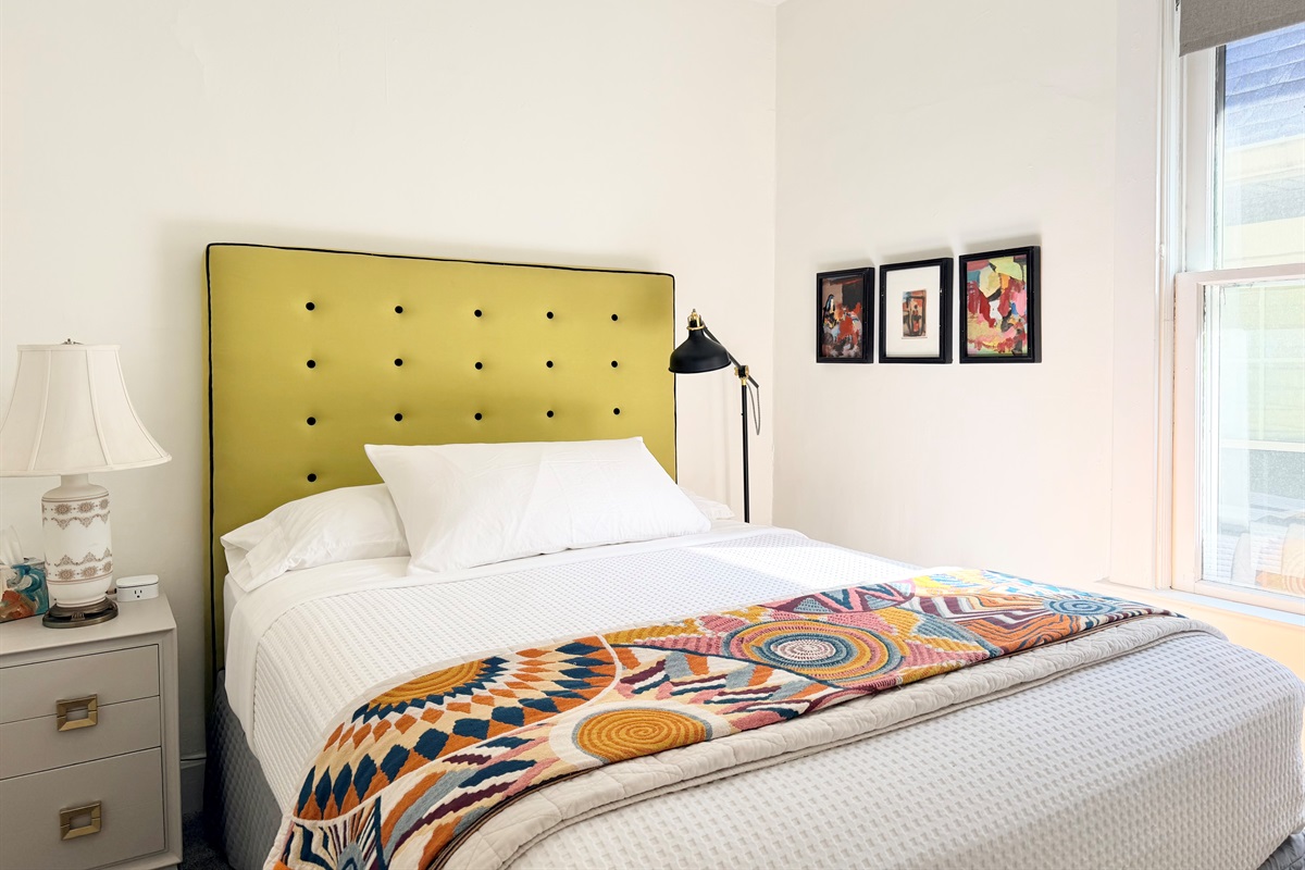 Queen bed with luxury cotton linens, plush mattress, blackout shades, bedside table, soft lighting, ceiling fan & wireless charging station — our quietest room for deep, restful sleep