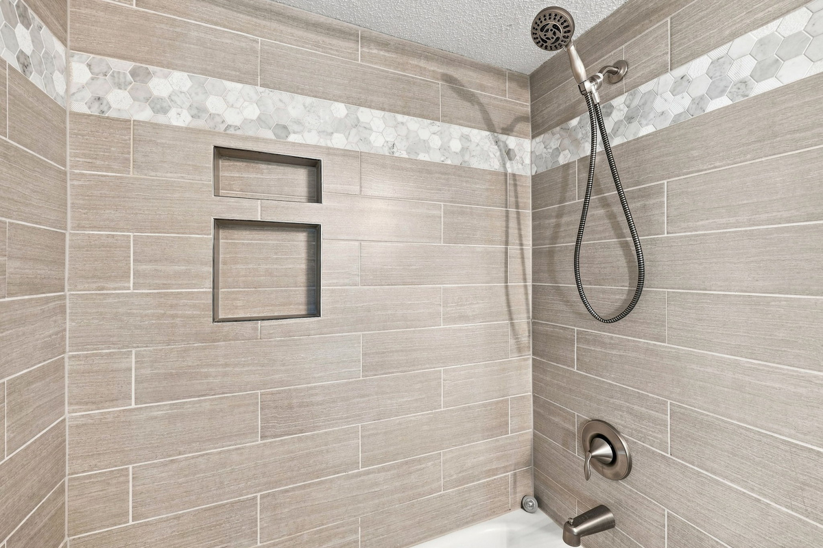 Neutral-toned tile surround outlining a functional bathtub and shower setup with modern plumbing fixtures.