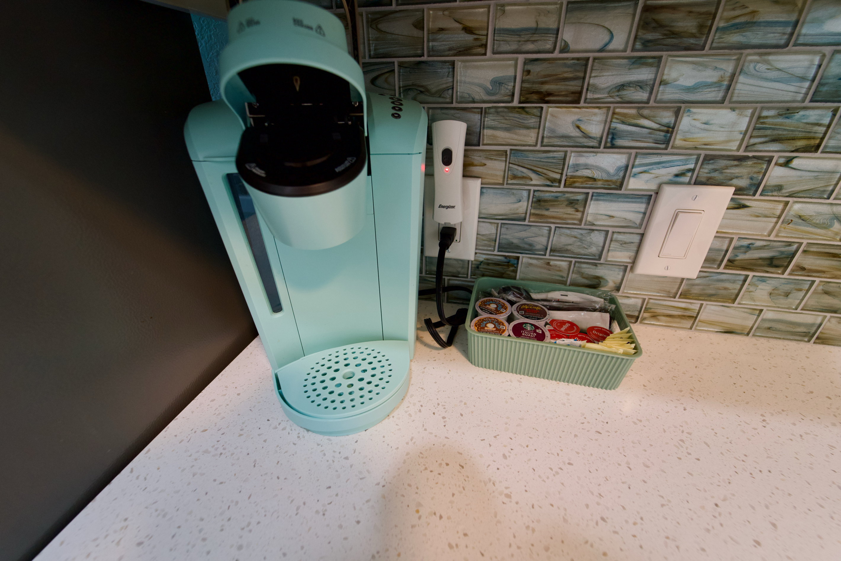 Start your day right with a beachy teal Keurig, a selection of coffee, tea, and decaf, plus sugar, creamer, and 16oz cups—all set on a stunning stone countertop with a coastal backsplash.