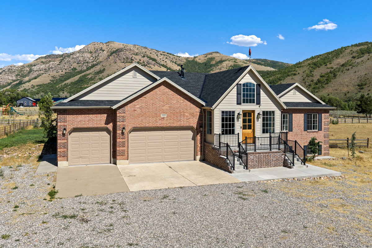 The home welcomes guests with a stately entrance, expansive driveway, and a serene setting framed by open land and mountain surroundings.