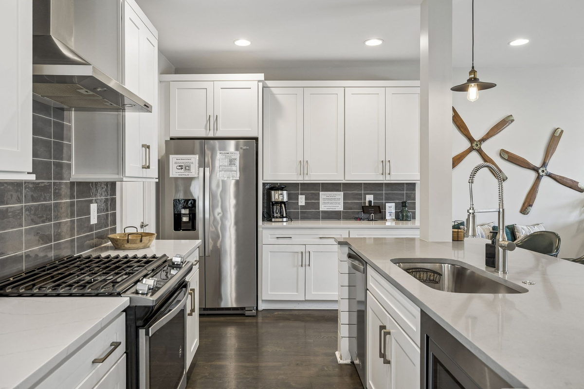 Full gourmet setup with stainless steel appliances, gas range, and large center island - Chic pendant lights, neutral tile backsplash, and extra counter space for easy prep - Wine and snack board welcome you into this stylish, functional culinary space