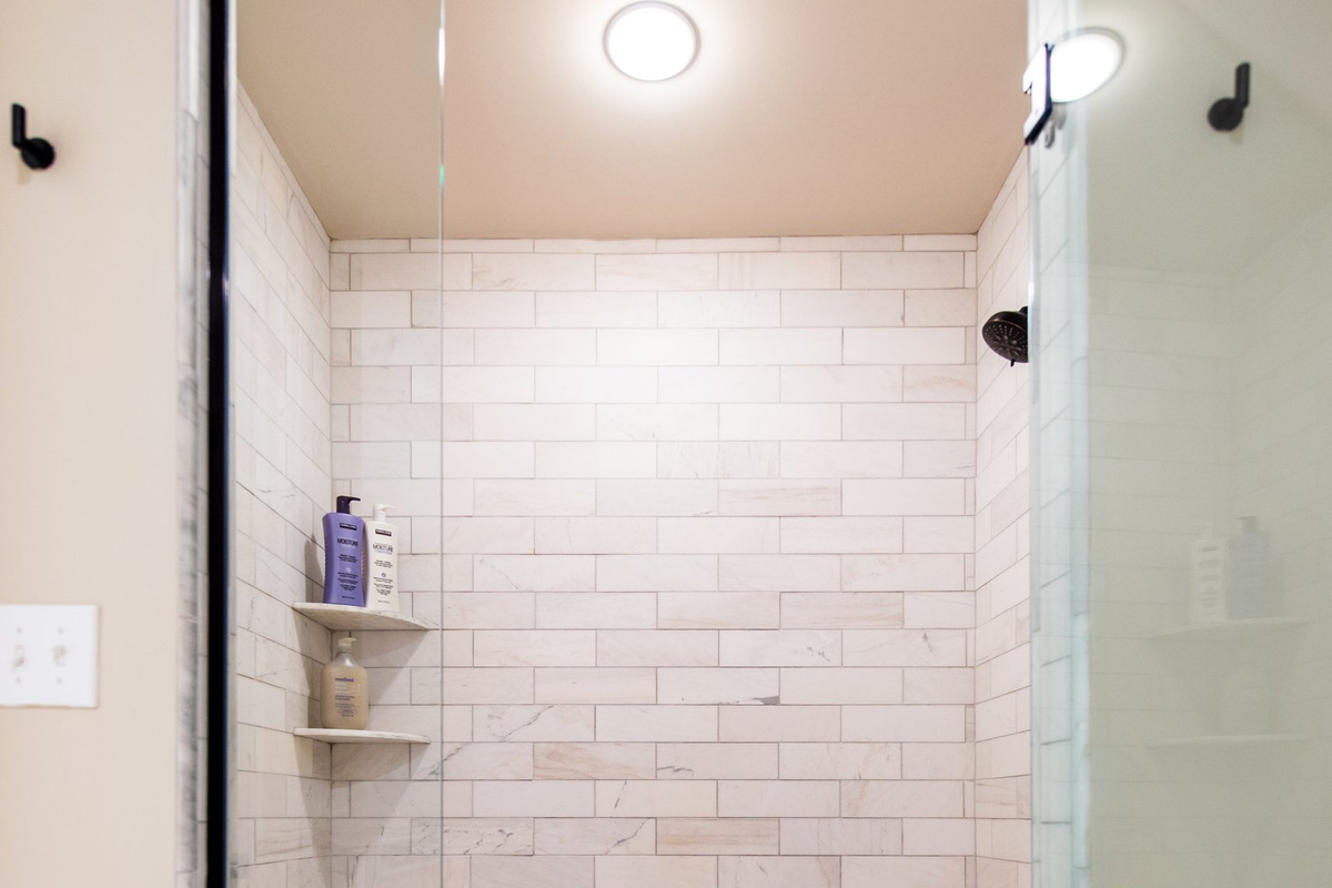 A glass-enclosed walk-in shower finished in marble subway tile.