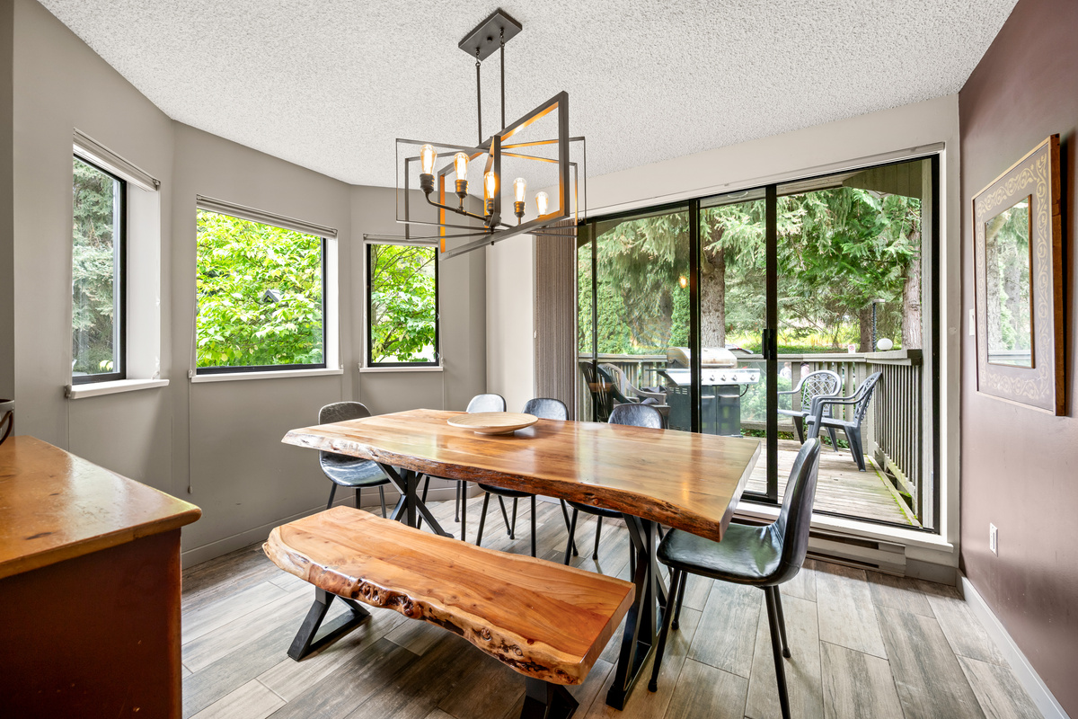 Dining room with a wood table, bench seating, and large bay windows and a slider to the private forest-view deck.