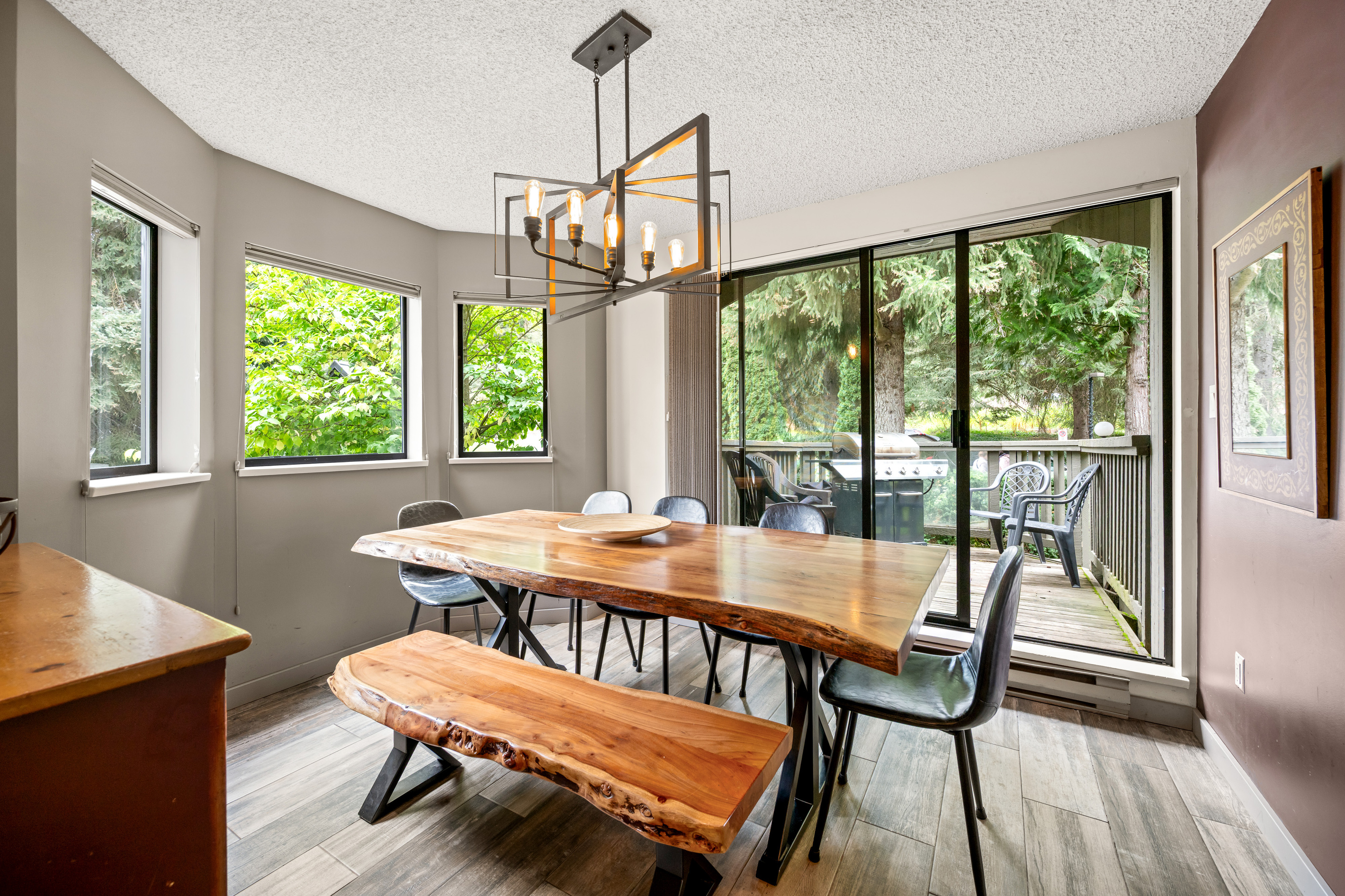 Dining room with a wood table, bench seating, and large bay windows and a slider to the private forest-view deck.