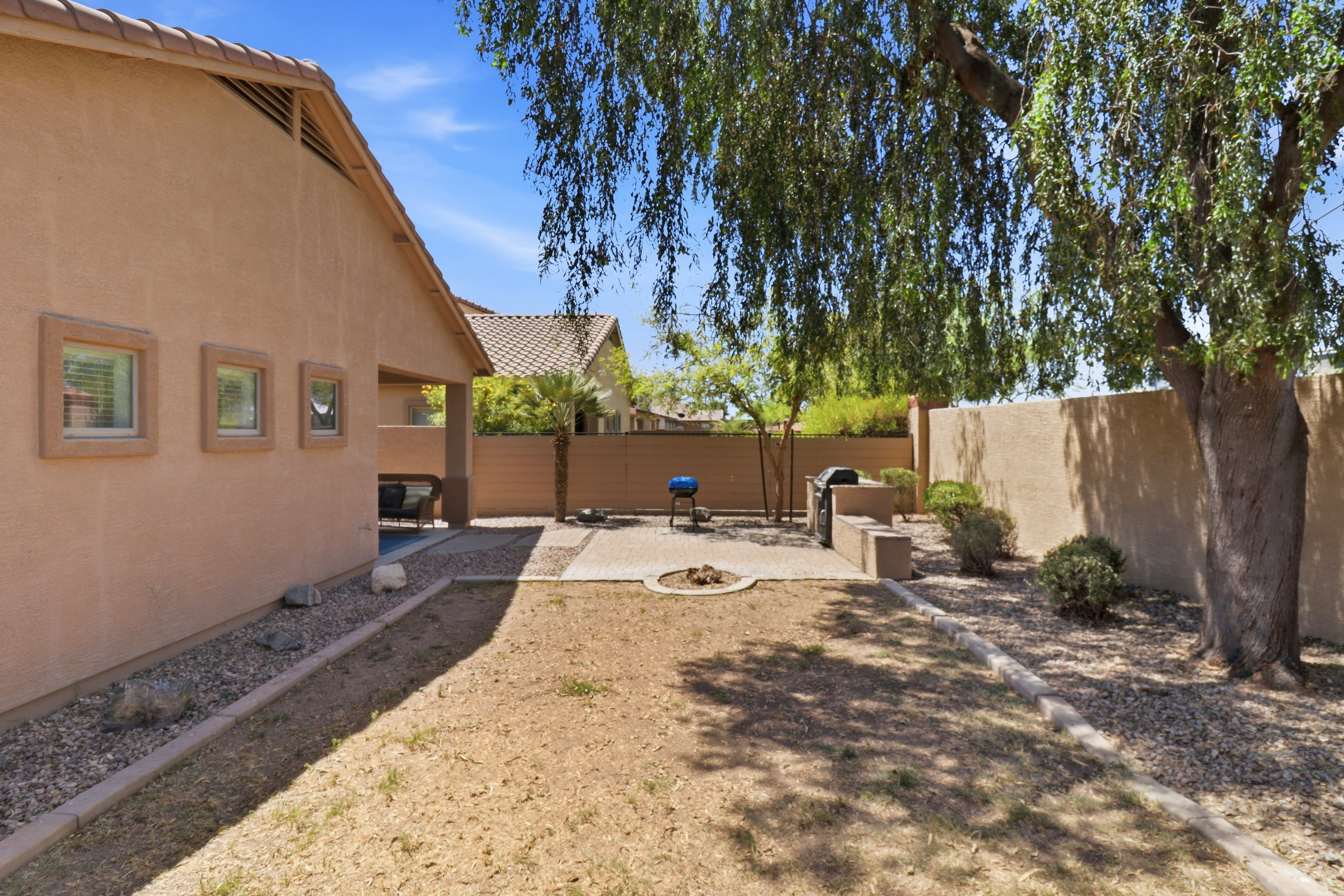 Fenced backyard with shade from the tree, a BBQ grill, and space to spend time outside.
