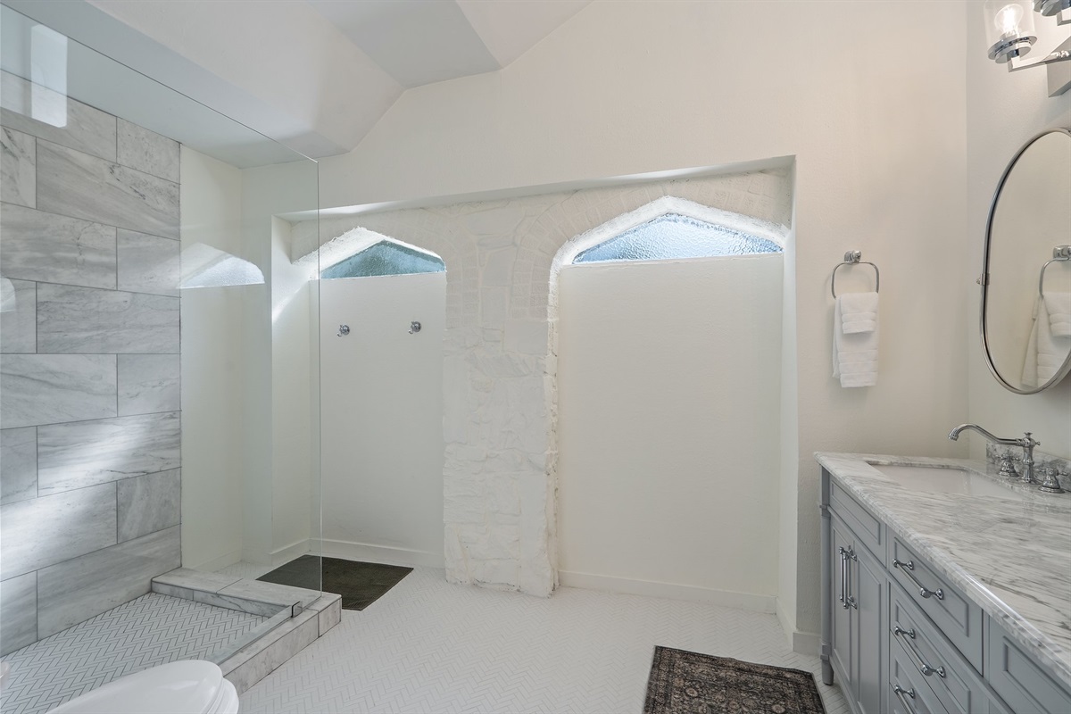 Bathroom 1 walk-in shower with floor-to-ceiling tile surround and arched ceiling detail. Stocked with Ginger Lily Farms shampoo, conditioner, and shower gel. Fresh towels, hairdryer, and essentials provided.
