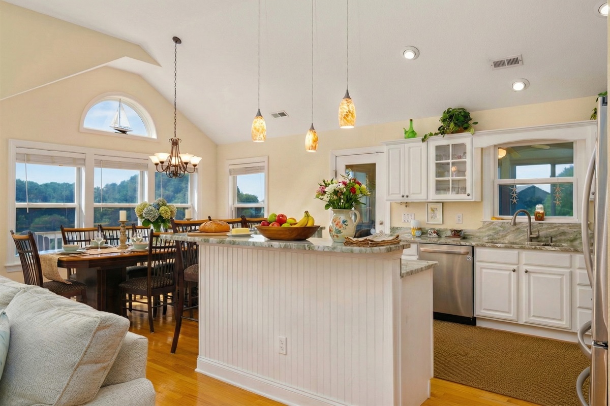 A sun-filled, open-concept kitchen and dining area featuring stainless steel appliances, a spacious breakfast bar, and a large dining table for group meals.