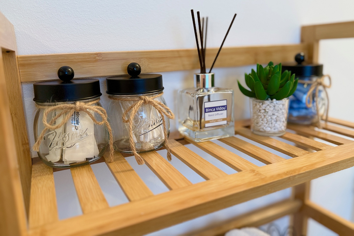 Bathroom shelf includes decorative storage jars and a reed diffuser.