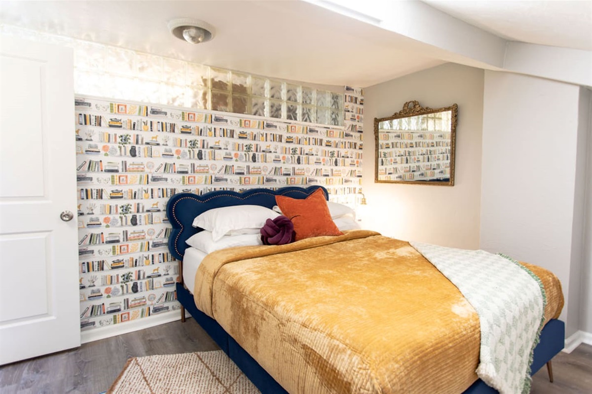 Indulge in ultimate comfort in this stylish bedroom, featuring a plush queen bed adorned with luxury linens. The unique bookshelf wallpaper adds a touch of character and sophistication, creating a cozy yet chic retreat. Enjoy the soft glow of the bed