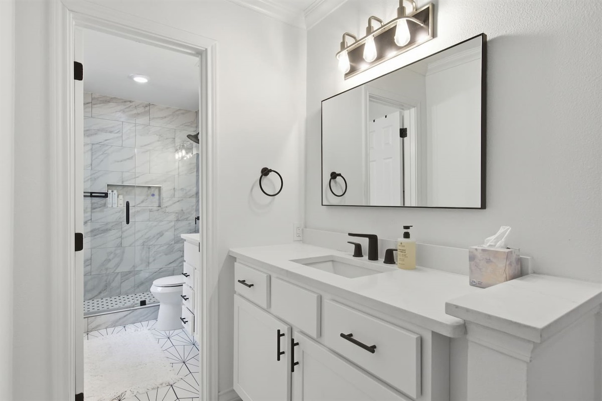 Modern full bathroom with rain shower, double vanity, large mirror, bright lighting, and fresh towels for guest comfort.