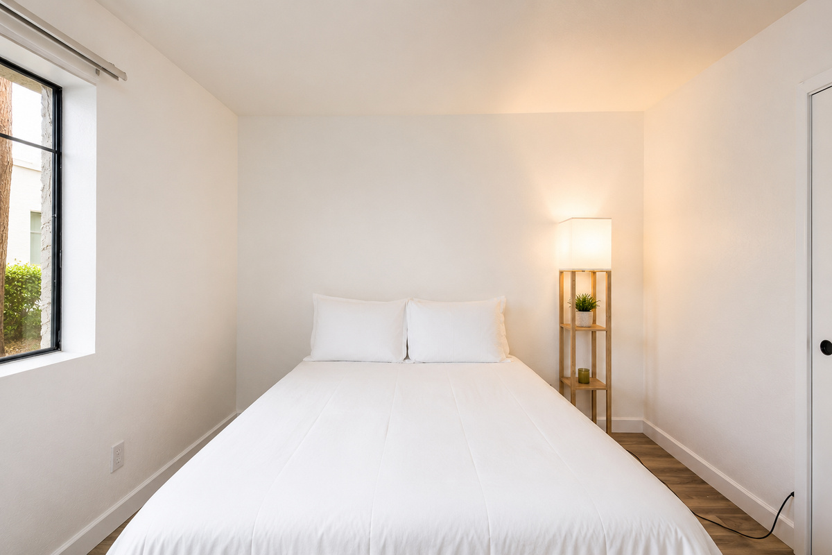 Simple queen bedroom with fresh white bedding, wood-look floors, closet space, and a floor lamp by the bed.