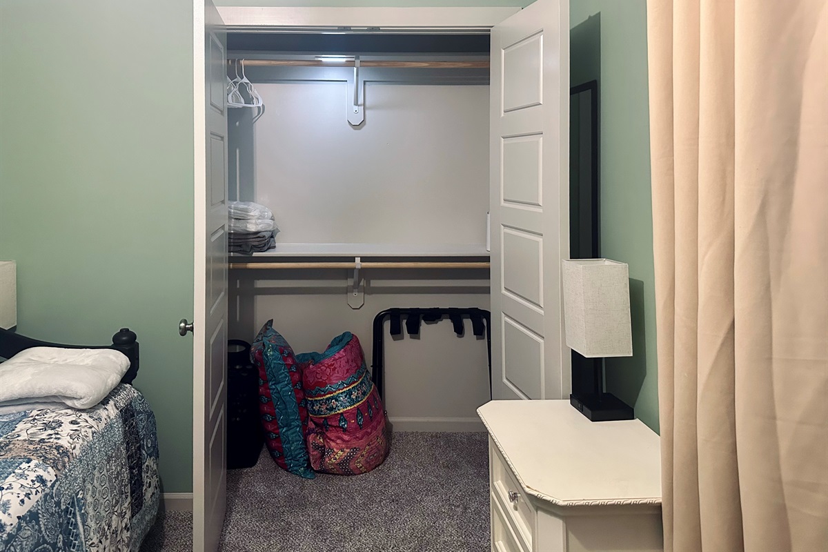 Third bedroom closet stocked with extra linens, additional comforter for the trundle, luggage rack, hangers, and laundry basket for convenient storage.