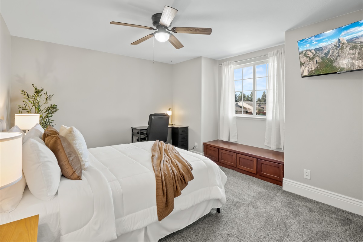 Spacious bedroom with plush carpeting, mounted TV, and a dedicated desk area—perfect for relaxing, working, or streaming your favorite shows.