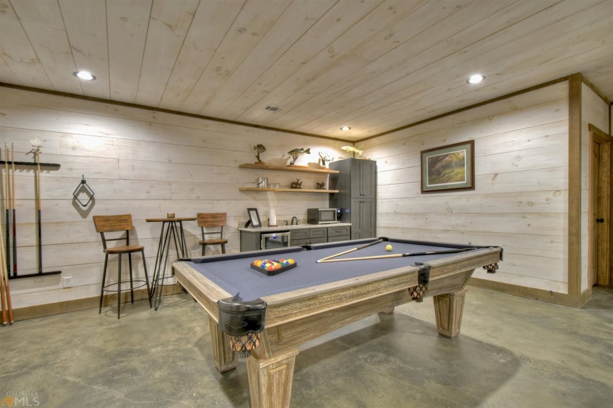 Pool table with wet bar is in main basement room with sitting table by pool table, other tables for board games, cards, etc.